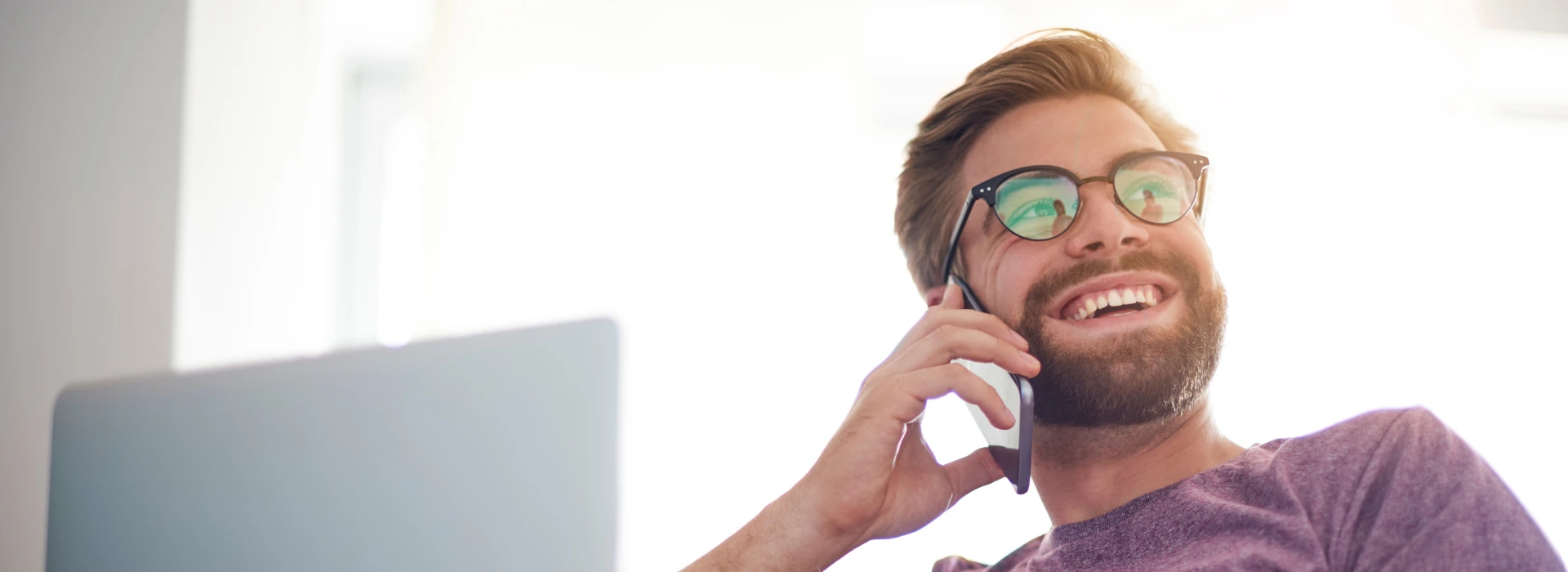 Smaidošs vīrietis ar progresīvajām brillēm runā pa mobilo telefonu